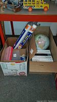 Two boxes containing assorted office supplies and a world globe in one box.