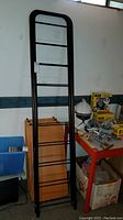 Full view of black metal frame with horizontal bars alongside wooden shelves and other items in background.
