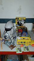 Overview photo showing Fisher Price yellow school bus, Woody doll, Star Wars helmet and figures, giant panda toy box, baseball trivia cards, hockey figures