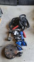 Photo showing coiled black battle ropes with red handles alongside varied dumbbells, kettlebells and weighted plates laid on the floor.