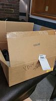 Closed cardboard box with 'Xbox 360' handwritten on side and auction label attached, showing contents inside but not detailed.