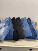 Seven pairs of girl jeans folded and displayed side by side showing various denim shades and styles.