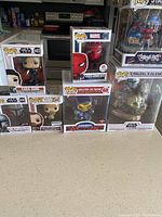 All seven Pop! collectible figures displayed on a counter in their original boxes. Figures are from Star Wars, Marvel, Masters of the Universe, and Street Art series. Spider-Man box shows damage on one corner.