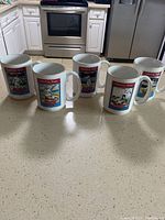 Five white ceramic coffee mugs arranged on kitchen counter, showing front illustrations related to Baseball Immortals.