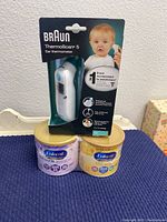 Photo showing two cans of Enfamil NeuroPro infant formula and Braun ThermoScan 5 ear thermometer sealed in retail packaging.