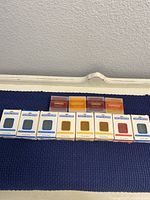 12 bar soap lot on a blue surface with 8 Papoutsanis bars and 4 Bath & Bloom bars.