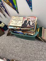 Photo of a large plastic bin filled with vinyl records stacked vertically and horizontally, showing album covers with classical and easy listening themes including a formal portrait of a man and choral music album.