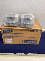 Two Purell NXT Space Saver 1L sanitizer dispensers on top of a box labeled Purell 2120-06