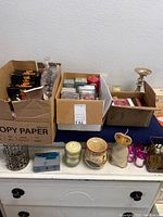 Boxes filled with various boxed and loose candles, twisted taper candles, and ceramic candle holders.