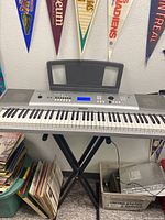 Full view of Yamaha DGX-230 digital piano with keyboard stand and book holder, various items around it.