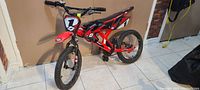 Photo of red and black kids bike from an angle showing front wheel, fender, and handlebars.