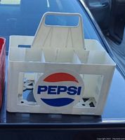 White plastic Pepsi carrier box with vintage logo and bottle compartments on a car trunk