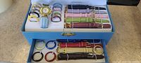Full set showing the gold-tone wristwatch with blue leather strap, multiple interchangeable leather bands in various colors, and plastic bezels/band holders in assorted colors.