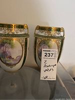Two matching antique Nippon vases with double handles, green and gold gilded decoration, handpainted pastoral scenes