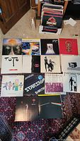 Overhead shot of ten vinyl record covers arranged on carpet with storage box visible