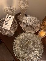Five pieces of clear cut glassware showing intricate cut patterns including starbursts, diamond and hobnail designs. Includes candy dish, various bowls, and tall vase.