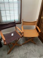 Two wooden frame directors chairs side by side, one with brown canvas, the other mustard canvas, both foldable with armrests.