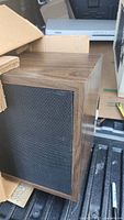 Wooden framed loudspeaker close-up showing dark wood grain and black mesh grille in good condition.