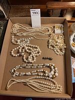 Full view of all necklaces, pearl pin, and earring backs in cardboard box.