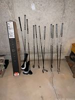 Eight clubs and two headcovers leaning against concrete wall, shipping box at left