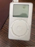 Front view of white Apple iPod Classic with click wheel and screen, dusty and used condition.