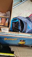 Photo showing a box with vinyl records and a partial view of a Jimmy Buffett album cover featuring a man in a yellow shirt and hat.
