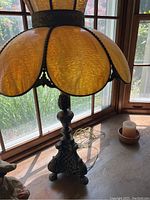Close-up of lamp shade and part of the base showing yellow-orange stained glass panels and ornate metal stand.
