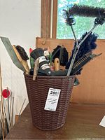 Woven-style brown plastic wastebasket holding various brushes and gardening tools on a shelf near a window