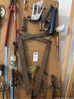 Various garage tools and right angle squares hanging on pegboard with some visible rust and wear