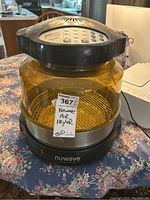 Side angle showing the air fryer with transparent yellow glass bowl, black base and top control unit, metal cooking rack inside bowl, product label affixed.