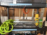 Green coiled expandable hose, livestock trap cage, Raid insect spray, and Nature's Defense animal repellent on a black shelving unit.