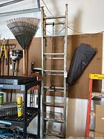 Full vertical view of large aluminum extension ladder leaning against pegboard with nearby tools and garage items.