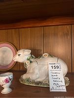 Photo of Meiselman ceramic lamb shaped tureen decorated with daisies sitting beside decorative egg holder and plate.