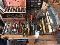 Overview of hand tools on workbench including pliers, screwdrivers, wrenches, hammers and metal toolbox.
