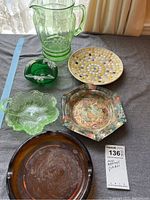 Full lot showing a green glass pitcher, two green ashtrays, mosaic dish, hexagonal folk art dish, and large brown carnival glass ashtray.