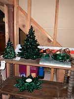 Photo showing the two ceramic Christmas trees in green with multi-colored bulbs, two ceramic candle holders, and extra bulbs on a wooden surface in a basement setting.