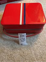 Closed red vinyl vintage suitcase with white and blue stripes on top, lying on carpet.