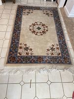 Full view of the cream background area rug with blue floral border and central medallion, showing overall design and fringe