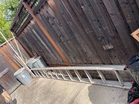Extended aluminum ladder leaning against a wooden fence on a concrete surface