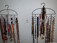Two metal hangers holding approximately 30 colorful costume jewelry necklaces made of beads, shells, wood, stone, and plastic displayed against a white wall.