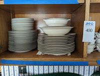 Stack of dinner plates, salad plates, dessert plates, soup bowls, dessert bowls, and platters on wooden shelving.