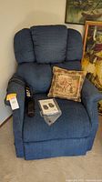 Blue Golden brand power lift and recline chair with patterned pillow on seat and remote controls resting on arm.