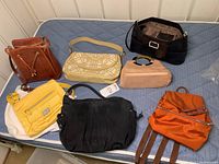 Seven purses in various colors and materials displayed on bed, showing overall collection
