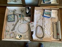 Wide view of various silver tone and sterling jewelry items arranged in two open boxes, showing necklaces, bracelets, and charms.