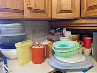 Wide view of kitchen counter with assorted Tupperware containers, pitchers, and storage items under cabinets