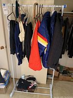Full view of clothing rack with winter jackets, pants, and gloves hanging, plus items below rack.