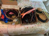 Photo of two boxes filled with various woman’s belts in leather, cloth, and metal materials laid on a bedspread