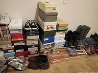Stack of shoe boxes and several pairs of shoes on floor including athletic shoes, sandals, boots, and casual shoes.