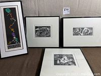 Three framed prints displayed together on a surface, including a tall colorful cartoon-style print and two smaller black and white prints.