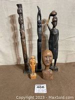 Five African wood carvings on neutral background, showing full figures and a head bust.